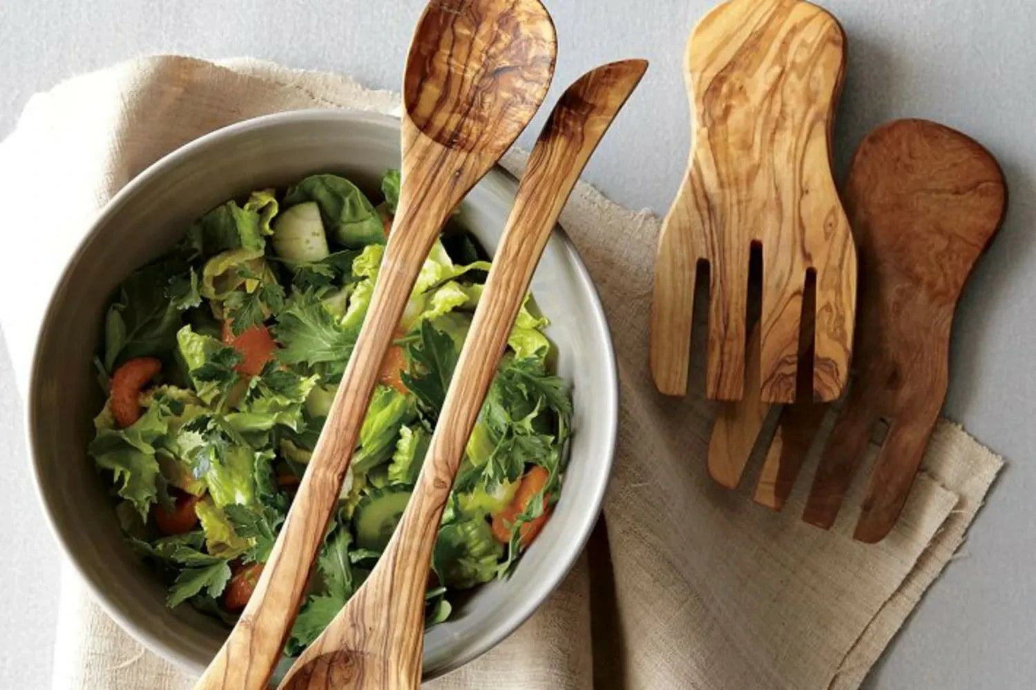 Wooden salad utensils with a bowl of salad on a neutral background