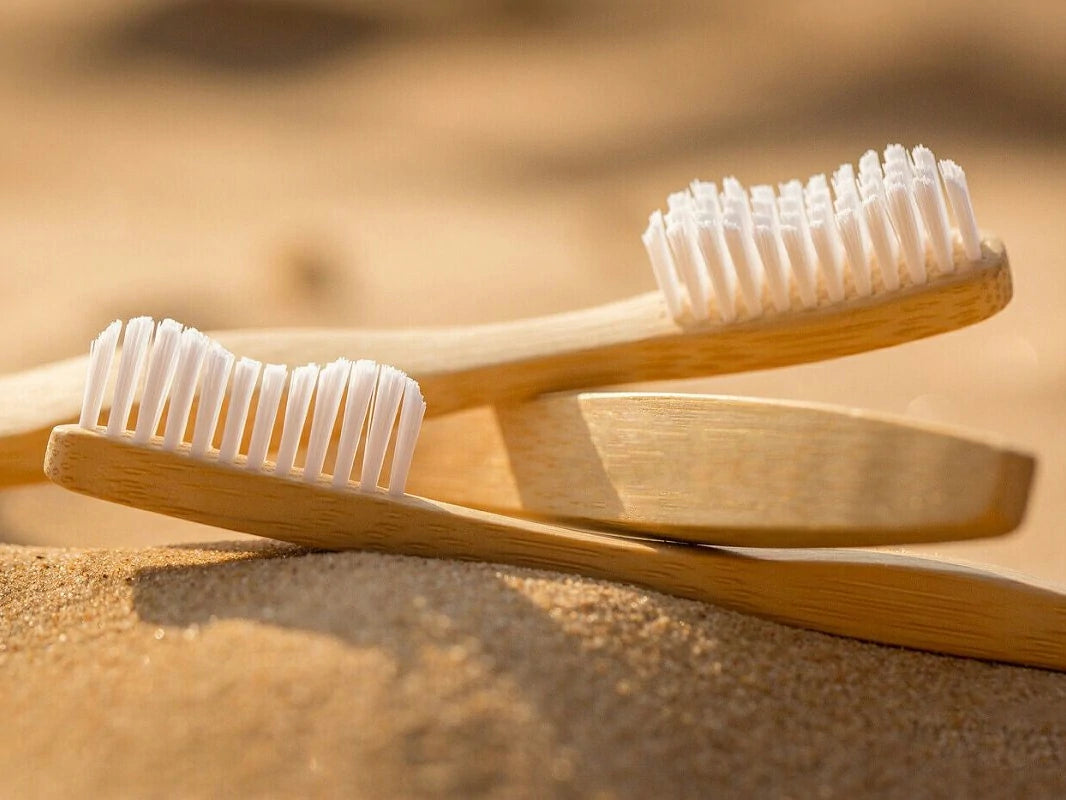 Two bamboo toothbrushes with white bristles on a sandy background