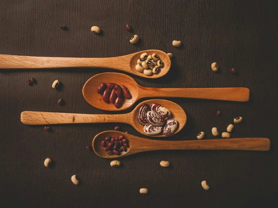 Wooden spoons filled with various seeds and beans on a dark surface